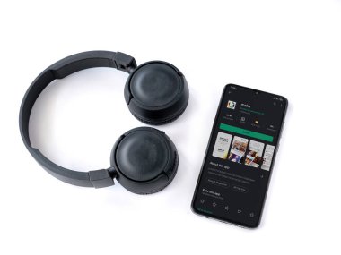 Lod, Israel - 8 Temmuz 2020: Mako app oyun mağazası sayfası ve beyaz arka planda kablosuz kulaklıkları olan siyah cep telefonu. Üst görünüm düzlüğü kopyalama alanı ile yatıyordu.