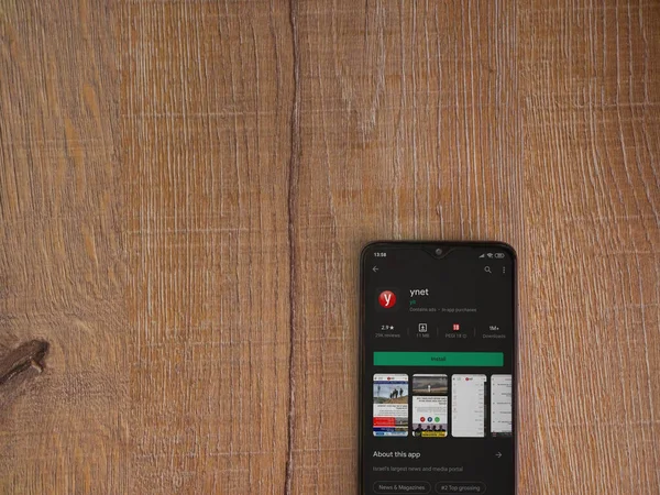Lod, Israel - 8 Temmuz 2020: ynet uygulama oyun mağazası sayfası ahşap arka planda siyah bir cep telefonunun ekranında. Üst görünüm düzlüğü kopyalama alanı ile yatıyordu.