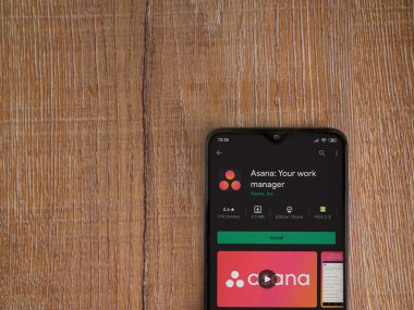 Lod, Israel - 8 Temmuz 2020: Asana uygulama oyun mağazası sayfası ahşap arka planda siyah bir cep telefonu ekranında. Üst görünüm düzlüğü kopyalama alanı ile yatıyordu.