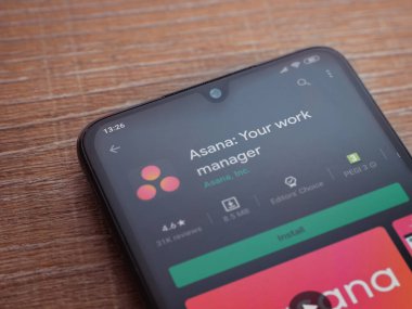 Lod, Israel - 8 Temmuz 2020: Asana uygulama oyun mağazası sayfası ahşap arka planda siyah bir cep telefonu ekranında. Üst görünüm düzlüğü kopyalama alanı ile yatıyordu.