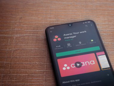 Lod, Israel - 8 Temmuz 2020: Asana uygulama oyun mağazası sayfası ahşap arka planda siyah bir cep telefonu ekranında. Üst görünüm düzlüğü kopyalama alanı ile yatıyordu.