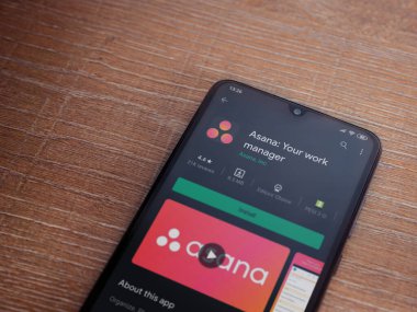 Lod, Israel - 8 Temmuz 2020: Asana uygulama oyun mağazası sayfası ahşap arka planda siyah bir cep telefonu ekranında. Üst görünüm düzlüğü kopyalama alanı ile yatıyordu.