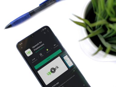 Lod, Israel - 8 Temmuz 2020: Modern minimalist ofis çalışma alanı ve beyaz arka planda Upwork for Freelancers uygulaması oyun sayfası olan siyah cep telefonu. Üst görünüm düzlüğü kopyalama alanı ile yatıyordu.