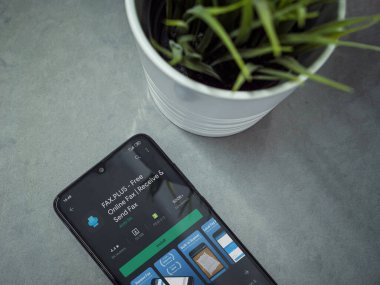 Lod, Israel - 8 Temmuz 2020: Modern minimalist ofis çalışma alanı ile siyah cep telefonu ve faks Plus uygulama oyun mağazası sayfası mermer arka planda. Üst görünüm düzlüğü kopyalama alanı ile yatıyordu.