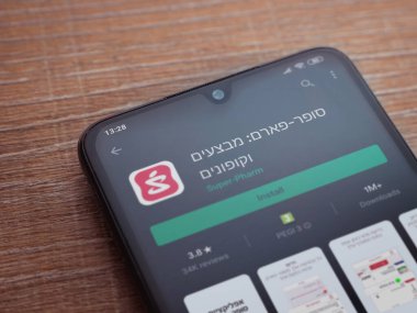 Lod, Israel - 8 Temmuz 2020: Süper Pharm uygulama oyun mağazası sayfası ahşap arka planda siyah bir cep telefonunun ekranında. Üst görünüm düzlüğü kopyalama alanı ile yatıyordu.