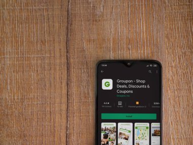 Lod, Israel - 8 Temmuz 2020: Groupon uygulaması oyun mağazası sayfası ahşap arka planda siyah bir cep telefonunun ekranında. Üst görünüm düzlüğü kopyalama alanı ile yatıyordu.