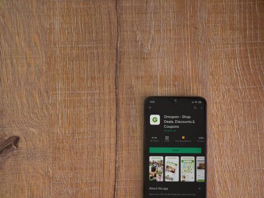 Lod, Israel - 8 Temmuz 2020: Groupon uygulaması oyun mağazası sayfası ahşap arka planda siyah bir cep telefonunun ekranında. Üst görünüm düzlüğü kopyalama alanı ile yatıyordu.