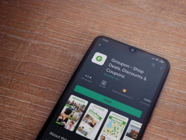 Lod, Israel - 8 Temmuz 2020: Groupon uygulaması oyun mağazası sayfası ahşap arka planda siyah bir cep telefonunun ekranında. Üst görünüm düzlüğü kopyalama alanı ile yatıyordu.