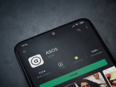 Lod, Israel - July 8, 2020: ASOS app play store page on the display of a black mobile smartphone on dark marble stone background. Top view flat lay with copy space. clipart