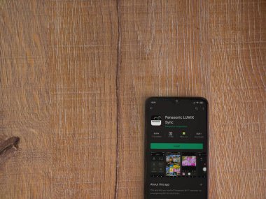 Lod, Israel - 8 Temmuz 2020: Panasonic LUMIX Sync uygulama oyun mağazası sayfası ahşap arka planda siyah bir cep telefonu görüntüsü. Üst görünüm düzlüğü kopyalama alanı ile yatıyordu.
