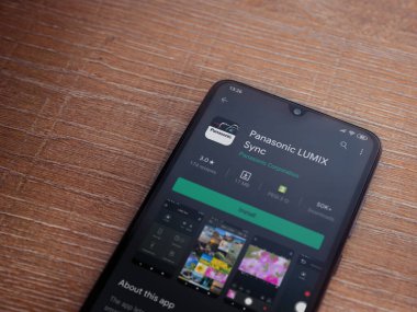Lod, Israel - 8 Temmuz 2020: Panasonic LUMIX Sync uygulama oyun mağazası sayfası ahşap arka planda siyah bir cep telefonu görüntüsü. Üst görünüm düzlüğü kopyalama alanı ile yatıyordu.