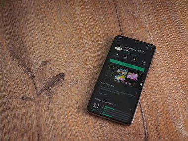 Lod, Israel - 8 Temmuz 2020: Panasonic LUMIX Sync uygulama oyun mağazası sayfası ahşap arka planda siyah bir cep telefonu görüntüsü. Üst görünüm düzlüğü kopyalama alanı ile yatıyordu.