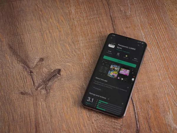 Lod, Israel - 8 Temmuz 2020: Panasonic LUMIX Sync uygulama oyun mağazası sayfası ahşap arka planda siyah bir cep telefonu görüntüsü. Üst görünüm düzlüğü kopyalama alanı ile yatıyordu.