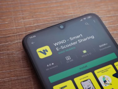 Lod, Israel - 8 Temmuz 2020: Rüzgâr uygulaması oyun mağazası sayfası ahşap arka planda siyah bir cep telefonunun ekranında. Üst görünüm düzlüğü kopyalama alanı ile yatıyordu.