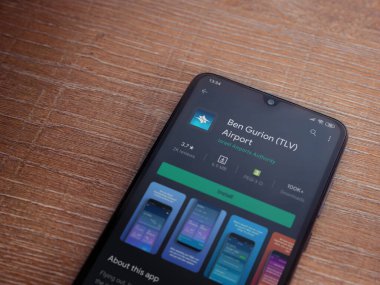 Lod, Israel - 8 Temmuz 2020: Ben Gurion Havalimanı uygulama oyun mağazası sayfası ahşap arka planda siyah bir cep telefonunun ekranında. Üst görünüm düzlüğü kopyalama alanı ile yatıyordu.