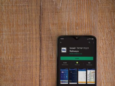 Lod, Israel - 8 Temmuz 2020: İsrail Demiryolları uygulama oyun mağazası sayfası ahşap arka planda siyah bir cep telefonunun ekranında. Üst görünüm düzlüğü kopyalama alanı ile yatıyordu.