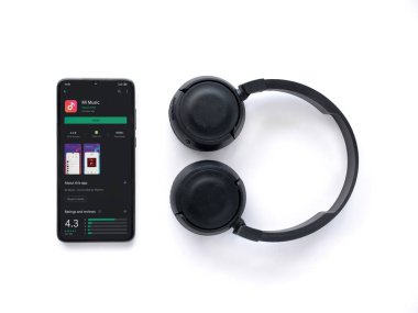 Lod, Israel - 8 Temmuz 2020: Siyah cep telefonu, Mi Music uygulama oyun mağazası sayfası ve beyaz arka planda kablosuz kulaklıklar. Üst görünüm düzlüğü kopyalama alanı ile yatıyordu.
