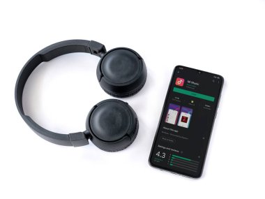 Lod, Israel - 8 Temmuz 2020: Siyah cep telefonu, Mi Music uygulama oyun mağazası sayfası ve beyaz arka planda kablosuz kulaklıklar. Üst görünüm düzlüğü kopyalama alanı ile yatıyordu.