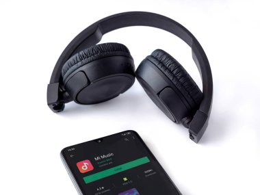 Lod, Israel - 8 Temmuz 2020: Siyah cep telefonu, Mi Music uygulama oyun mağazası sayfası ve beyaz arka planda kablosuz kulaklıklar. Üst görünüm düzlüğü kopyalama alanı ile yatıyordu.