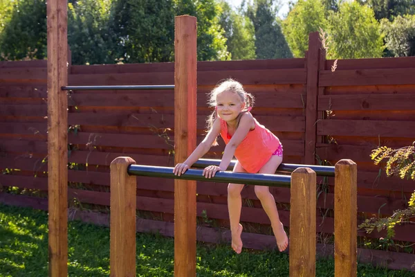 Klein meisje zittend op parallelle bars buiten — Stockfoto