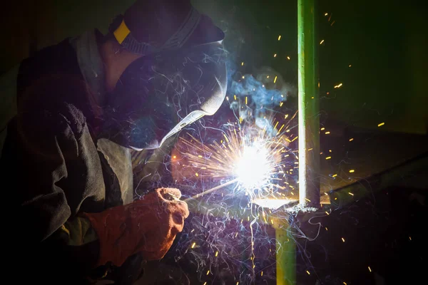 A welder at work.  Sparks flying. Welder in mask at work. Profession of a welder. Sparks around. Welding metal. Dark background. Bright light.