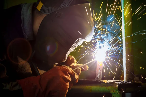 A welder at work.  Sparks flying. Welder in mask at work. Profession of a welder. Sparks around. Welding metal. Dark background. Bright light.