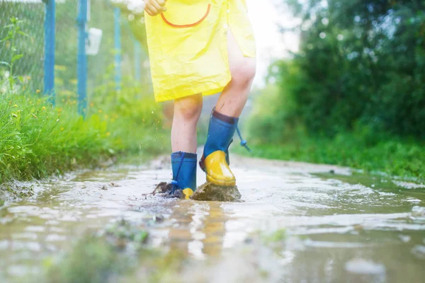 child\'s feet in a rubber boot in a puddle