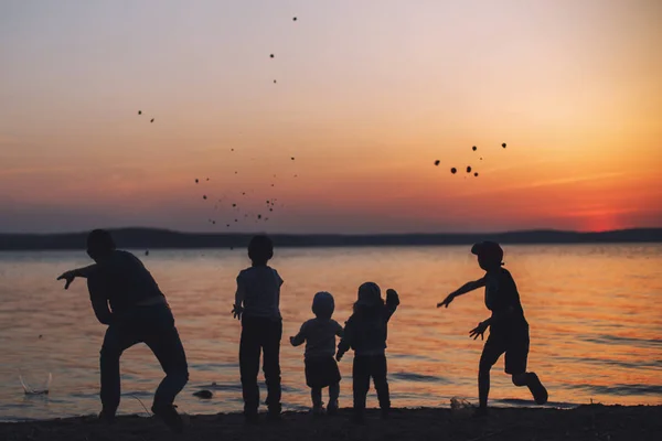 people at sunset throwing stones into the water. dad with children