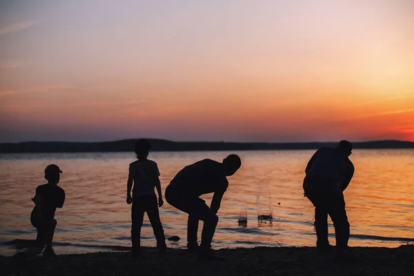 people at sunset throwing stones into the water