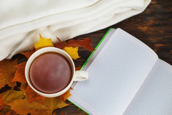 cup of coffee or tea with golden autumn leaves, plaid and notepad on a wooden background .top view. Fall concept.Autumn composition