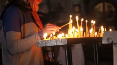 Kadının elini tutar ve kilisede bir mum koyar. Tapınaktaki insanlar Tanrı'ya dua. Birçok yanan mumlar.