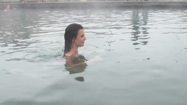 Геотермальный курорт. Женщина отдыхает в бассейне с горячей водой. Девушка наслаждается бассейном с открытой дверью в теплой минеральной воде 25fps — стоковое видео