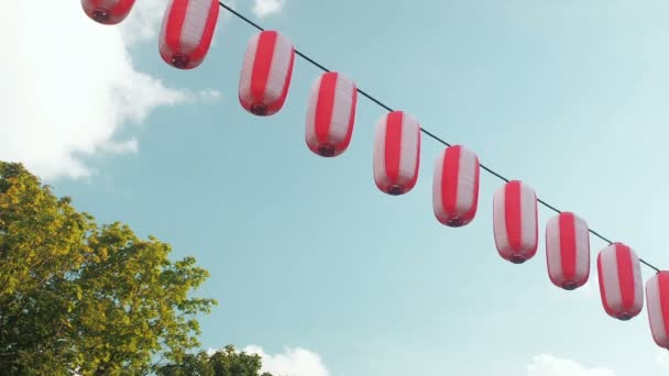 Papier rood-witte Japanse lantaarns Chochin opknoping op de blauwe hemelachtergrond en bomen — Stockvideo