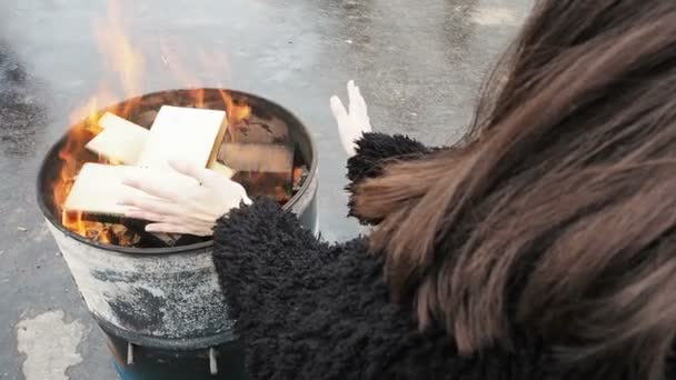 Mujer frotándose las manos frente a la chimenea en llamas. Chica se está calentando durante el invierno de fuego en un barril redondo — Vídeo de stock