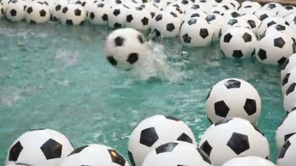 Muchas bolas de fútbol blanco y negro de fondo. Pelotas de fútbol nadando en agua pura. Una bola cae al agua creando un aerosol — Vídeo de stock