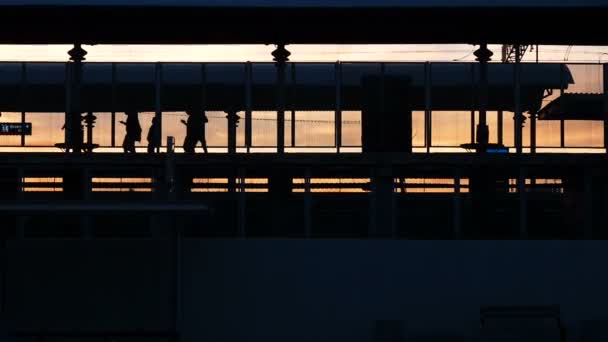 地下鉄駅、日没時に、プラットフォームの上を歩いての鉄道車両を残して人々 に入力鉄道のシルエット。鉄道駅のシーン: 帰国の人、 — ストック動画