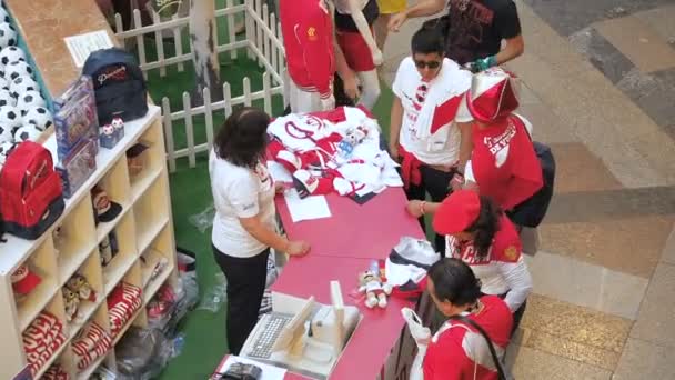 MOSCÚ, RUSIA - 5 de agosto de 2018: Los turistas compran uniformes oficiales de futbolistas como souvenirs en el punto de venta de la tienda deportiva en GUM, Moscú. Mujer probándose una camisa olímpica. El vendedor explica a — Vídeos de Stock