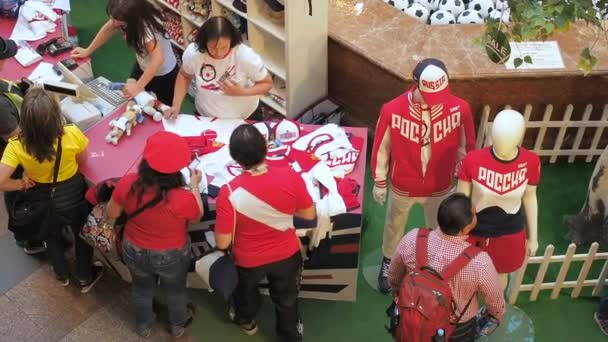 MOSCA, RUSSIA - 5 AGOSTO 2018: I turisti acquistano uniformi ufficiali per i giocatori di calcio come souvenir nel punto vendita del negozio di articoli sportivi a GUM, Mosca. Un venditore mostra ai turisti una cosa su un manichino che — Video Stock