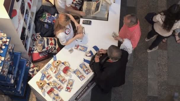 Moscow, Oroszország - 2018. augusztus 5.: Turisták vásárolni hivatalos ajándéktárgyak - Zabivaka játék a pont-ból Kiárusítás sport áruház gumi, Moszkva. A videó került sor, a fenti — Stock videók