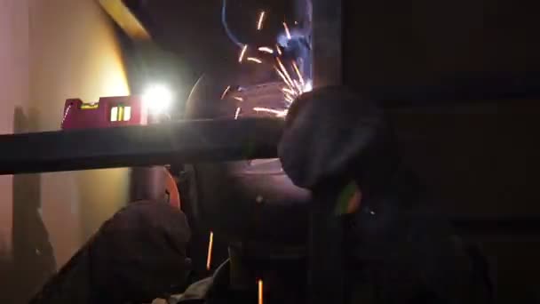 Spawacz pracownik wykonuje skok spawania. Spawacz pracownik wykonuje proces spawanie konstrukcji metalowych. Iskrami z maszyna do spawania. Spawacz spoin profile metalowe na drugim piętrze pomieszczeniu — Wideo stockowe