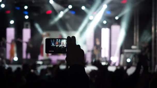 Hand hält Rekord Videokamera Smartphone Live-Konzert Performance Aufnahme Foto Musik Band Silhouetten tanzende Menschen applaudieren erhobenen Händen nach oben Menge applaudiert Rhythmus Musik Musiker auf der Bühne durchführen — Stockvideo