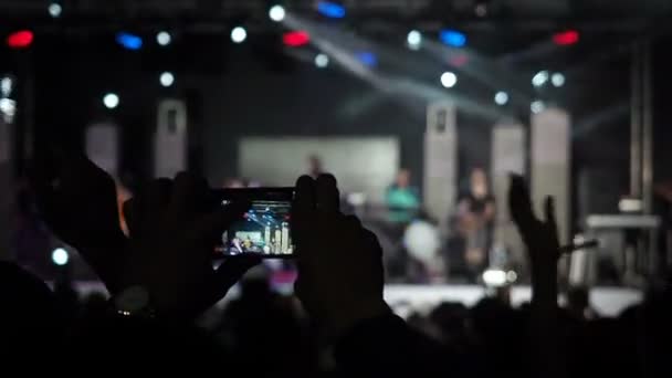 Männliche Hand hält Rekord Videokamera Zoom Smartphone Live-Konzert Performance Aufnahme Foto Musik Band Silhouetten tanzende Menschen applaudieren erhobenen Händen nach oben Menge applaudiert Rhythmus Musik Musiker — Stockvideo