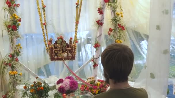 Man gently swing on swing idols of Radha and Krishna statue for begging the blessing on Jhulan Yatra fest — Stock Video