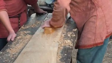 Uçakla bir ahşap çalışma Ortaçağ pamuklu giysiler içinde bir marangoz. Adam el ile bir ahşap tahta bir uçakla Hews