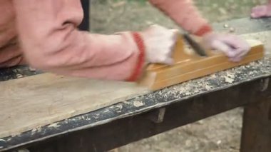 Uçakla bir ahşap çalışma Ortaçağ pamuklu giysiler içinde bir marangoz. Adam el ile bir ahşap tahta bir uçakla Hews