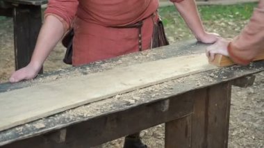 Uçakla bir ahşap çalışma Ortaçağ pamuklu giysiler içinde bir marangoz. Adam el ile bir ahşap tahta bir uçakla Hews