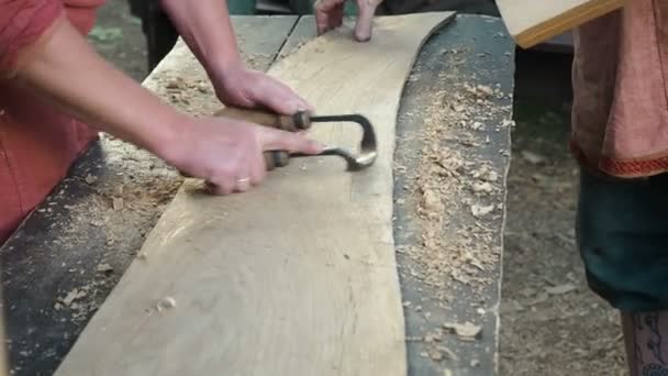 Плотник в средневековой хлопчатобумажной одежде, работающий с чернильным ножом или рисовавший ножик, бритье или бритье ножа - это инструменты для резки на деревянной доске. Столярные изделия из древесины лиственных пород. Процесс принятия решений — стоковое видео