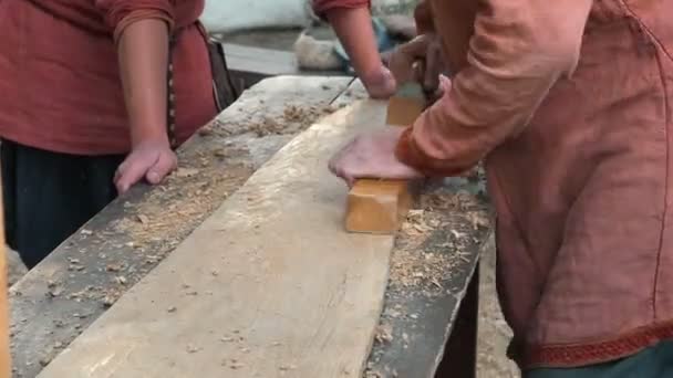 Carpinteiro em Roupas de Algodão Medieval Trabalhando com uma Madeira de Avião. Homem manualmente Hews uma placa de madeira com um avião — Vídeo de Stock