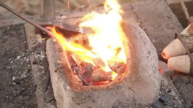 Demirci kütük bir kil Fırında sıcak kömürlerin üzerinde tutar. demir metal kılıç imalatı yürüyen forge Isıtma demirci