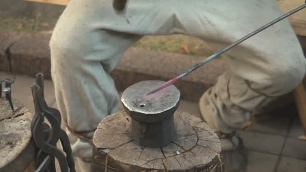 The blacksmith in the production process of metal products handmade on the openair workshop. Blacksmith strikes with a hammer on metal. Hands of a blacksmith with red-hot billet close up — Stock Video